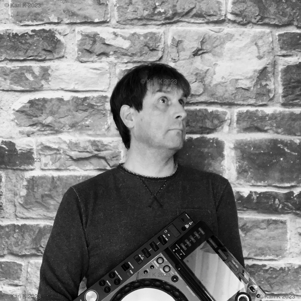 Valokuva henkilöstä nojaamassa kiviseinää vasten. Hänellä on sylissään tiskijukan levysoitin.